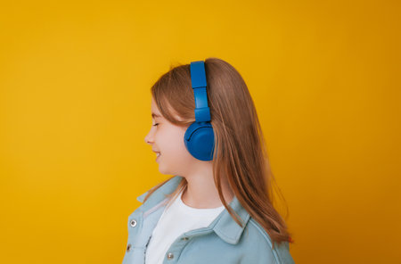 A young girl 11-13 years old in headphones listens to music and dances in the studio on a yellow backgroundの写真素材