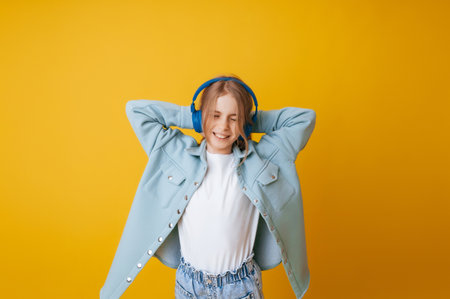 A young girl 11-13 years old in headphones listens to music and dances in the studio on a yellow backgroundの写真素材