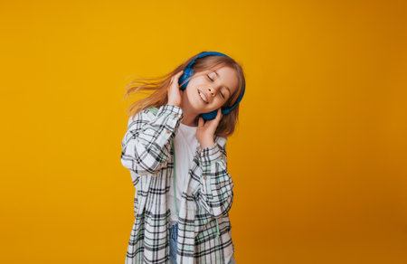 A young girl 11-13 years old in headphones listens to music and dances in the studio on a yellow backgroundの写真素材