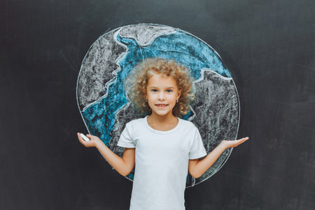 A cute little girl stands with her back and draws a planet on the board. the child holds his hands like a house above the planet.の写真素材