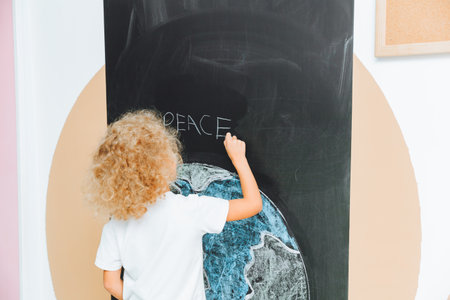 A cute little girl stands with her back and draws a planet on the board. the child holds his hands like a house above the planet.の写真素材