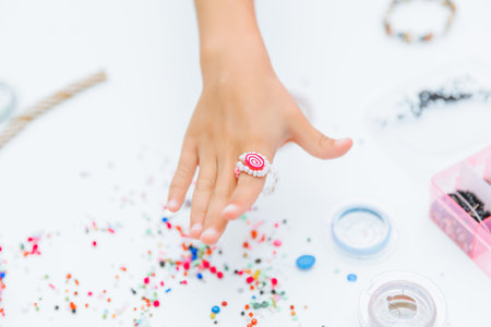Cute little blonde girl making bead jewelry at a table in the roomの写真素材