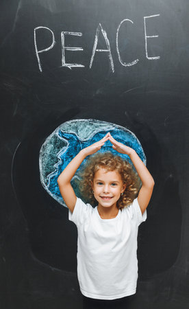 A cute little girl stands with her back and draws a planet on the board. the child holds his hands like a house above the planet.の写真素材