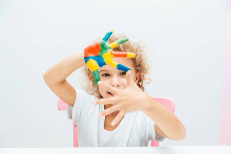 little blonde girl shows her hands painted with multi-colored paint on a white background.の写真素材