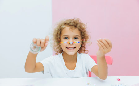 Cute little blonde girl making bead jewelry at a table in the roomの写真素材