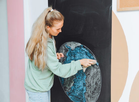 Planet Earth drawing with chalk on a blackboard. hand with chalk. girl student draws our land on the blackboard with chalk.の写真素材