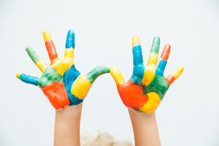 little blonde girl shows her hands painted with multi-colored paint on a white background.の写真素材