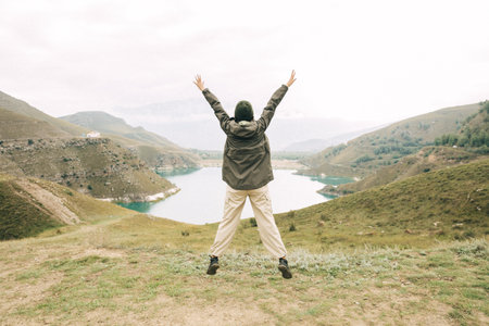 A cheerful girl is jumping against the backdrop of a mirror lake and mountains. Soft focus. Caucasusの写真素材