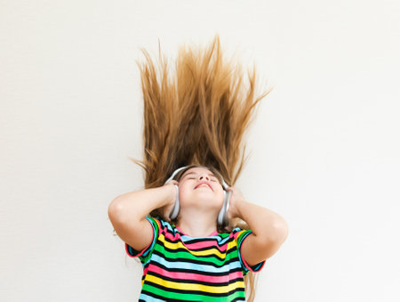 An energetic girl wearing headphones listens to music on a gray background in the studio. She wears a striped T-shirt. Long hair flies from movement.の写真素材