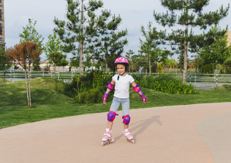 A little curly-haired girl rollerskates within the necessary facilities in the city. In a helmet and...