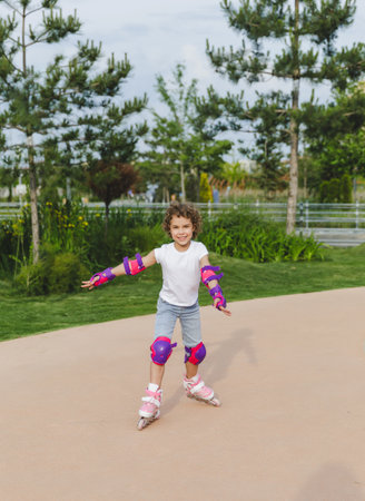 A little curly-haired girl rollerskates within the necessary facilities in the city. In a helmet and...