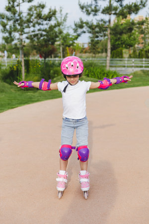 A little curly-haired girl rollerskates within the necessary facilities in the city. In a helmet and...