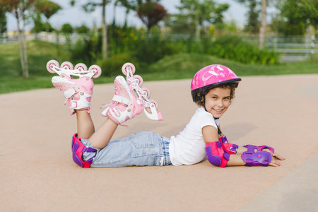 A little curly-haired girl sits in a roller-skating helmet and armbands.