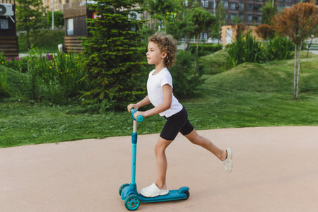 A little curly-haired girl rides a scooter in a city park.の写真素材