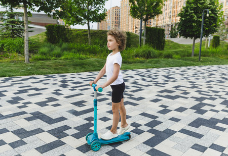 A little curly-haired girl rides a scooter in a city park.の写真素材