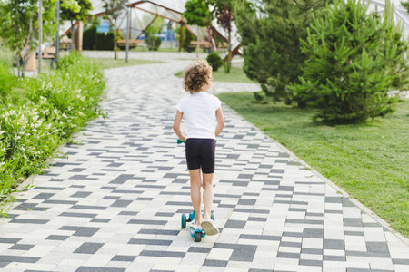 A little curly-haired girl rides a scooter in a city park.の写真素材