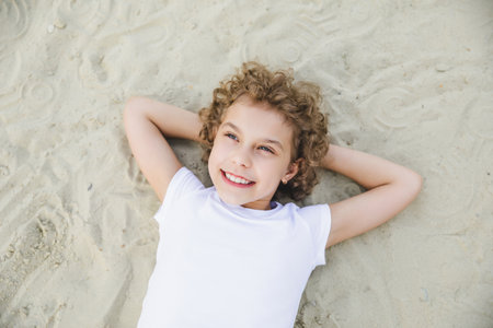 little curly blonde girl lies on the sand and smiles.summer portraitの写真素材