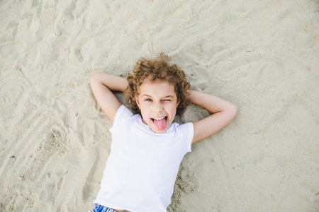 little curly blonde girl lies on the sand and smiles.summer portrait