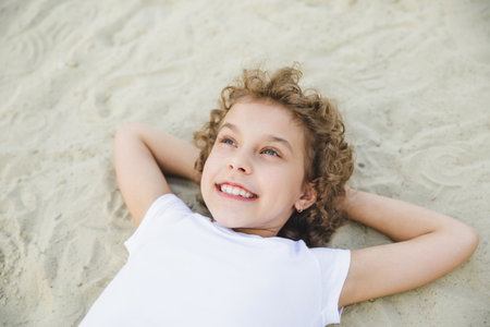 little curly blonde girl lies on the sand and smiles.summer portrait