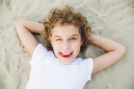 little curly blonde girl lies on the sand and smiles.summer portraitの写真素材