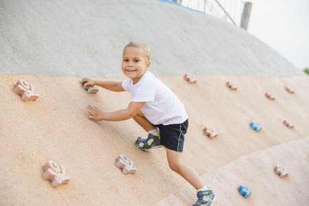 little boy climbing stone wall on playground. sport life conceptの写真素材