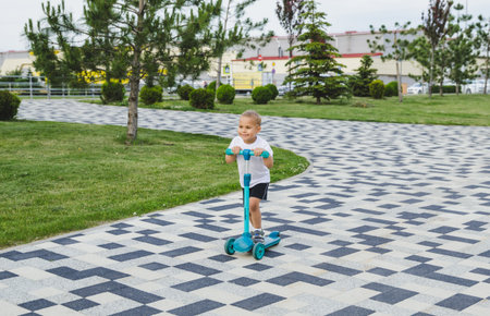 A boy of 4-5 years old rides a scooter in a city park.の写真素材