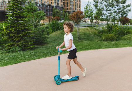 A little curly-haired girl rides a scooter in a city park.の写真素材