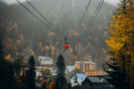 Red gondola cabin transports tourists over the mountain village of Dombay, surrounded by misty peaks...