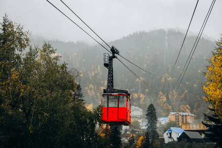 Red gondola cabin transports tourists over the mountain village of Dombay, surrounded by misty peaks and golden autumn forest in the Caucasusの写真素材