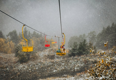 Colorful chairlifts carrying uphill in Dombay, surrounded by autumnal trees under a heavy dusting of early season snowの写真素材