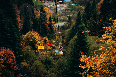 Colorful chairlifts carrying uphill in Dombay, surrounded by autumnal trees under a heavy dusting of early season snowの写真素材