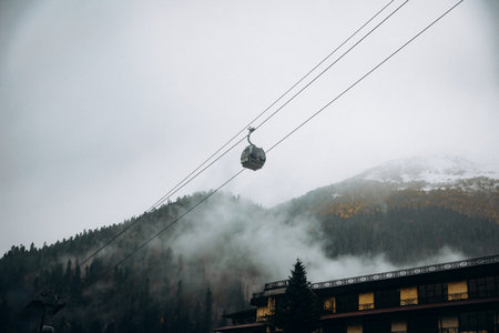 Gondola cabins move across the foggy Dombay sky during an early snow, showcasing the contrast...