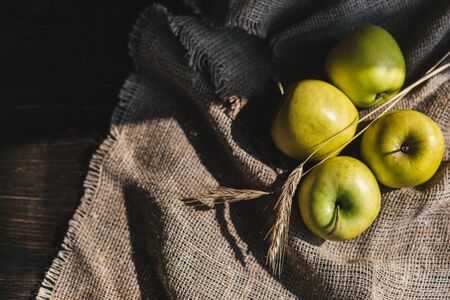 Ripe green apples on a rustic cloth and wooden table with spikeletsの写真素材