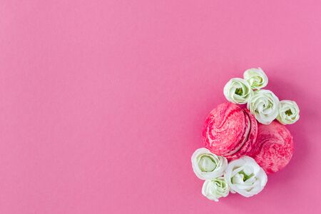 Two pink French macarons with white flowers on pink background. Flat lay, place for text.の写真素材