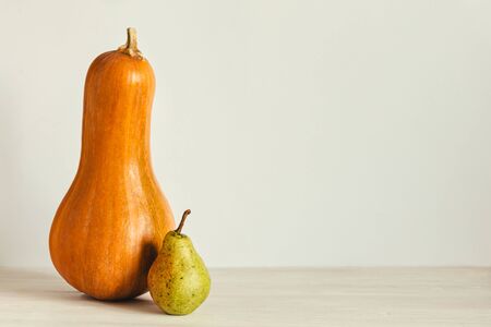 Ripe organic  pumpkin and pear on a pastel beige background. Minimal concept for Thanksgiving card or background. Place for text.の写真素材