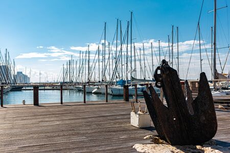 Old rusty anchor on embankment near Marina. Bright blue sky and skyscapers on background. Tel Aviv city, Israel.の写真素材