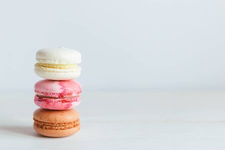 Three French macarons on a white wooden table. Multicolored macarons. White background. Minimal concept, place for text.の写真素材