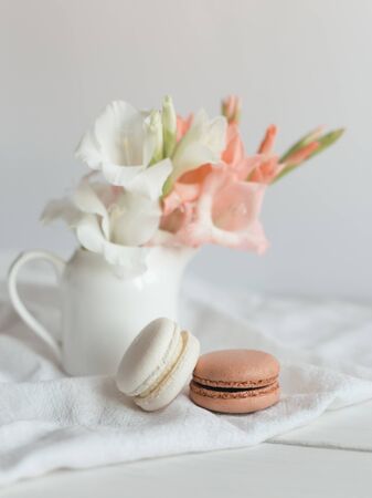 Two pastel French macarons and flowers in a jar on a white background. Cream and chocolate macarons.の写真素材