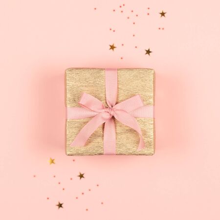 Golden gift box with pink bow on the pink background with sparkles. Holiday concept. の写真素材