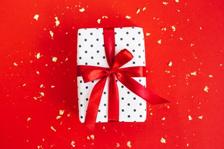 Gift box wrapped in black polka-dot white paper with red bow on red background with golden sparkles. Holiday concept.の写真素材