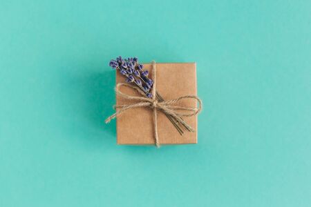 Craft gift box with small lavender bouquet on turquoise background. Holiday eco-friendly concept. Place for text. Flat lay.の写真素材