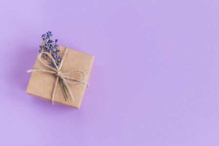 Craft gift box with small lavender bouquet on pastel violet background. Holiday eco-friendly concept. Place for text. Flat lay.の写真素材