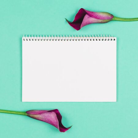 Beautiful violet calla lilies and notebook with blank page on turquoise background. Flat lay. Place for text.の写真素材