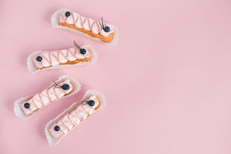 Tasty French eclairs with cream and fresh berries on pink pastel background. Set of delicious eclairs. Flat lay. Place for text.の写真素材
