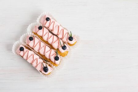 Tasty French eclairs with cream and fresh berries on white wooden table. Set of delicious eclairs.  Place for text. Flat lay.の写真素材