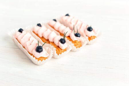 Tasty French eclairs with cream and fresh berries on white wooden table. Set of delicious eclairs. Selective focus. Place for text.の写真素材