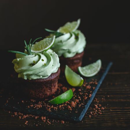 Tasty chocolate cupcake with buttercream icing and lime slices on a wooden table. Dark background.の写真素材