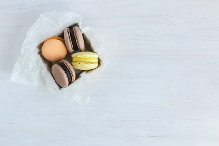 Tasty french macarons in gift box on a white wooden table. Pastel colors. Place for text.