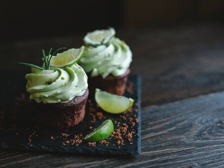 Tasty chocolate cupcake with buttercream icing and lime slices on a wooden table. Dark background.  Place for text.の写真素材