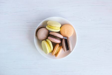 Tasty french macarons on a white plate. White wooden background, flat lay. Place for text.の写真素材